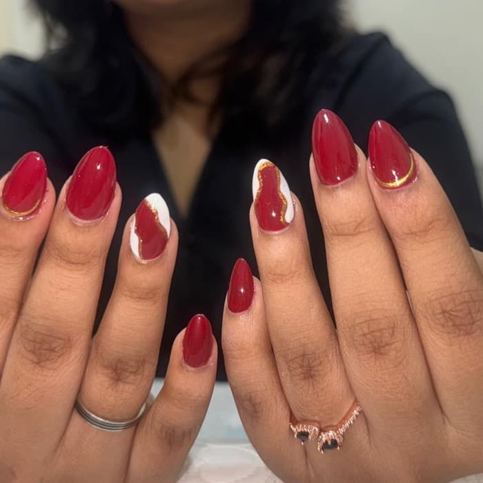 Red gel nails with white and gold accent art, done at Ezra's Nail Studio